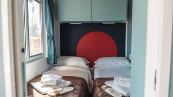 A compact bedroom with two beds, a red headboard, and a window with curtains.