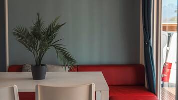 A compact room with a table, chairs, a red sofa, a potted plant, and an air conditioning unit.