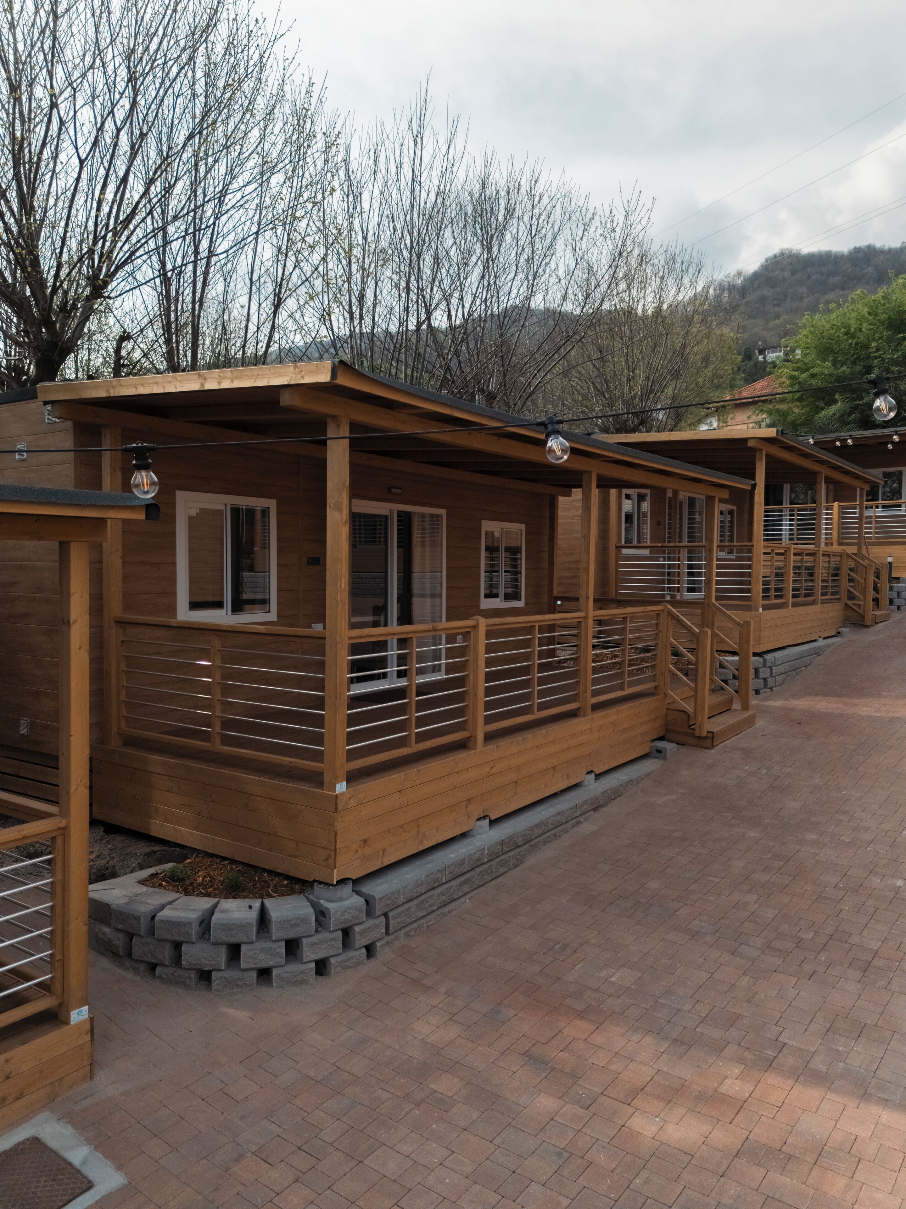 A row of wooden cabins with a covered walkway, wooden railings, and a brick pathway.