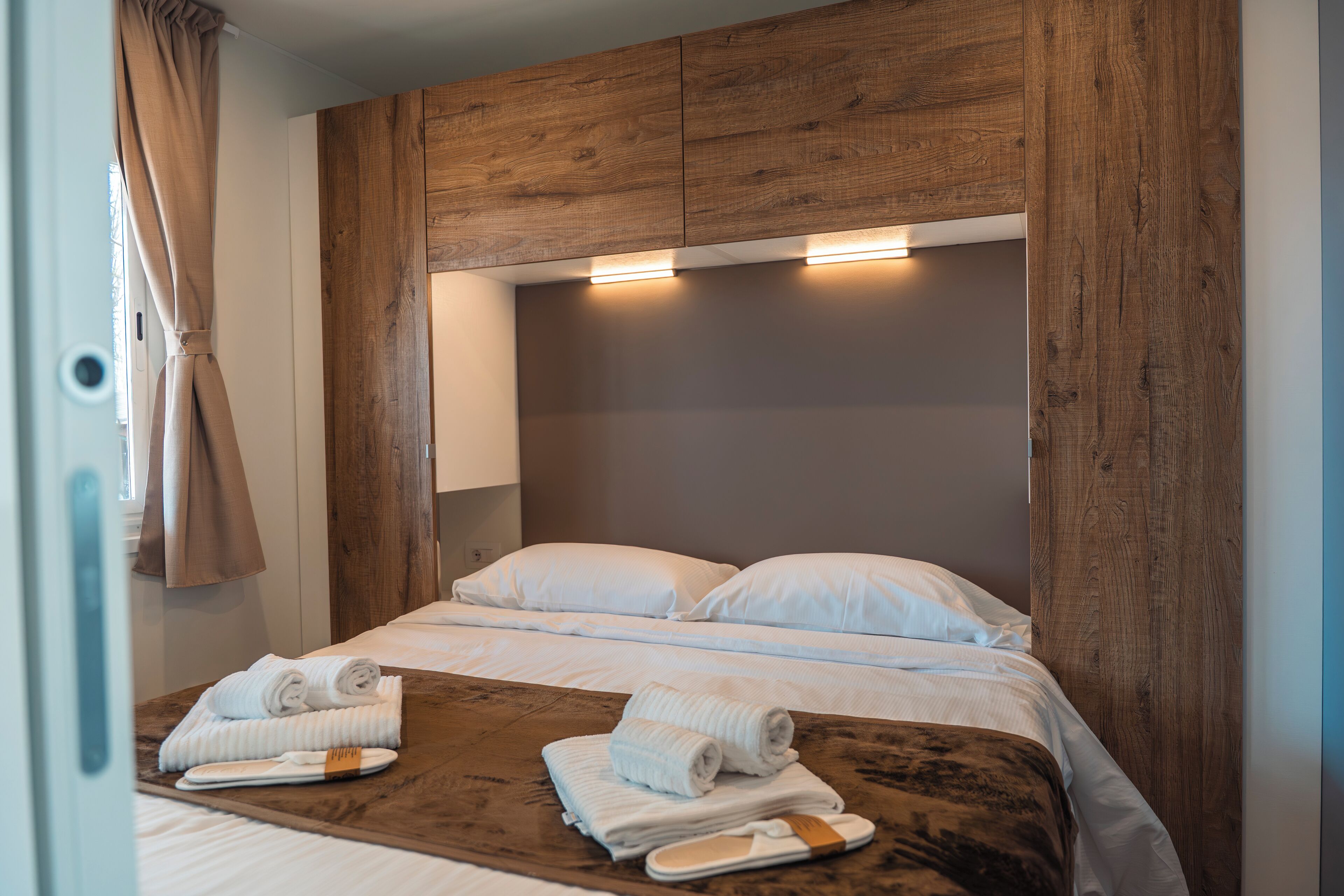 Ein Hotelzimmer mit einem hölzernen Kopfteil, zwei Betten mit weißen Laken und Handtüchern auf einem Holztablett.