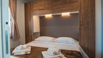 A hotel room with a wooden headboard, two beds with white linens, and towels on a wooden tray.