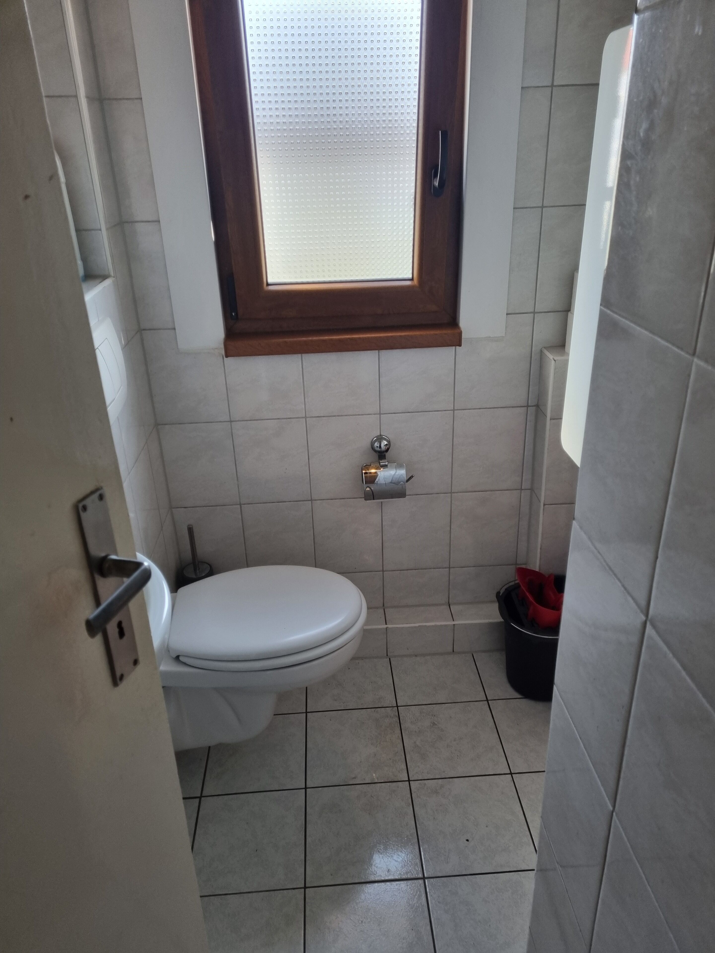 Et lille badeværelse med fliser, toilet, et vindue og en skraldespand.