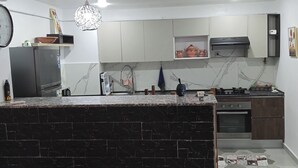 A modern kitchen with a central island, white cabinets, a stainless steel range hood, and a marble backsplash. - HOUCINE APARTMENT (Aïn El Turk)