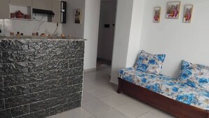 A living room with a sofa and a kitchen area with a stone backsplash. - HOUCINE APARTMENT (Aïn El Turk)