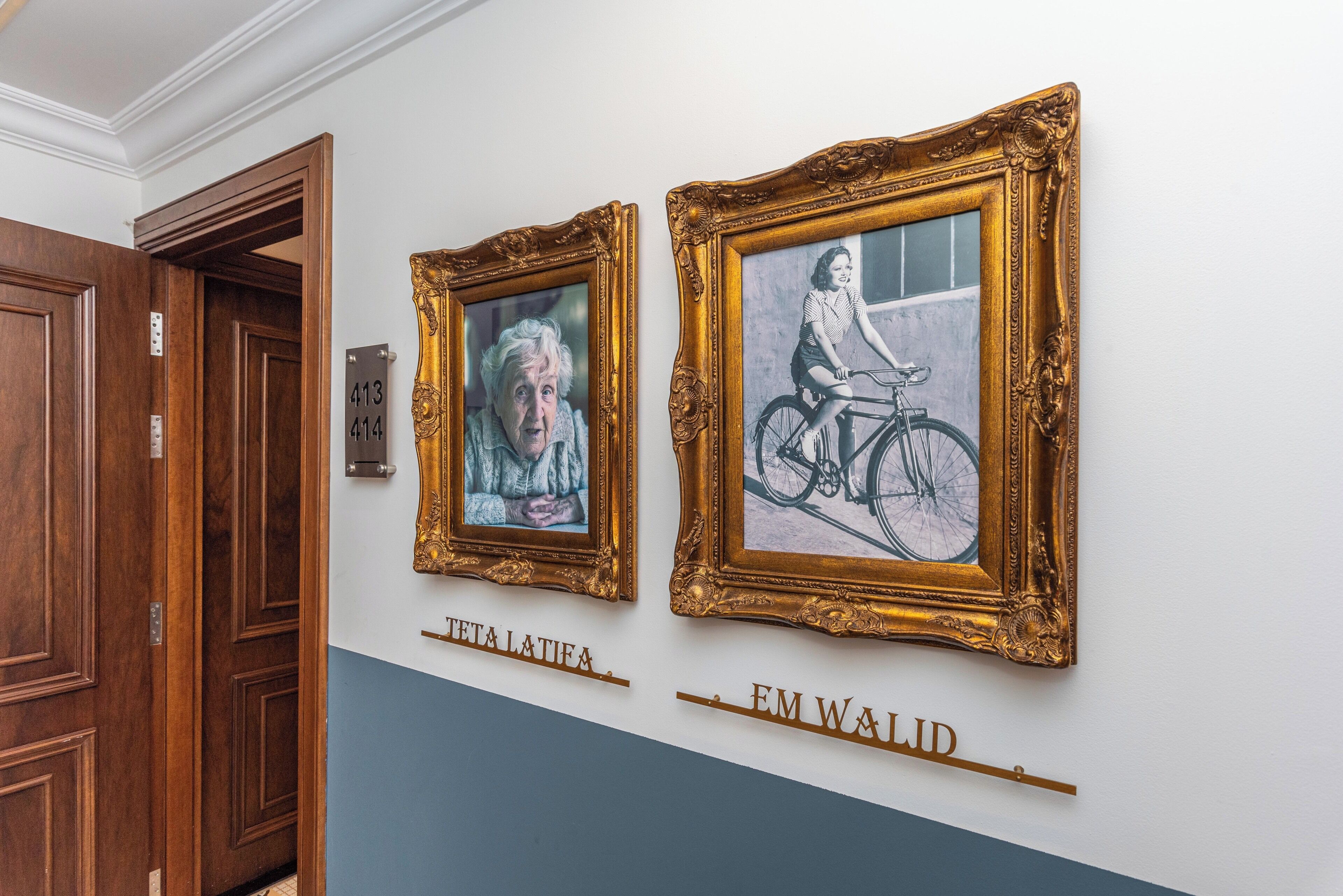 Two framed artworks on a wall with a blue and white color scheme, and a wooden door with a number plate.