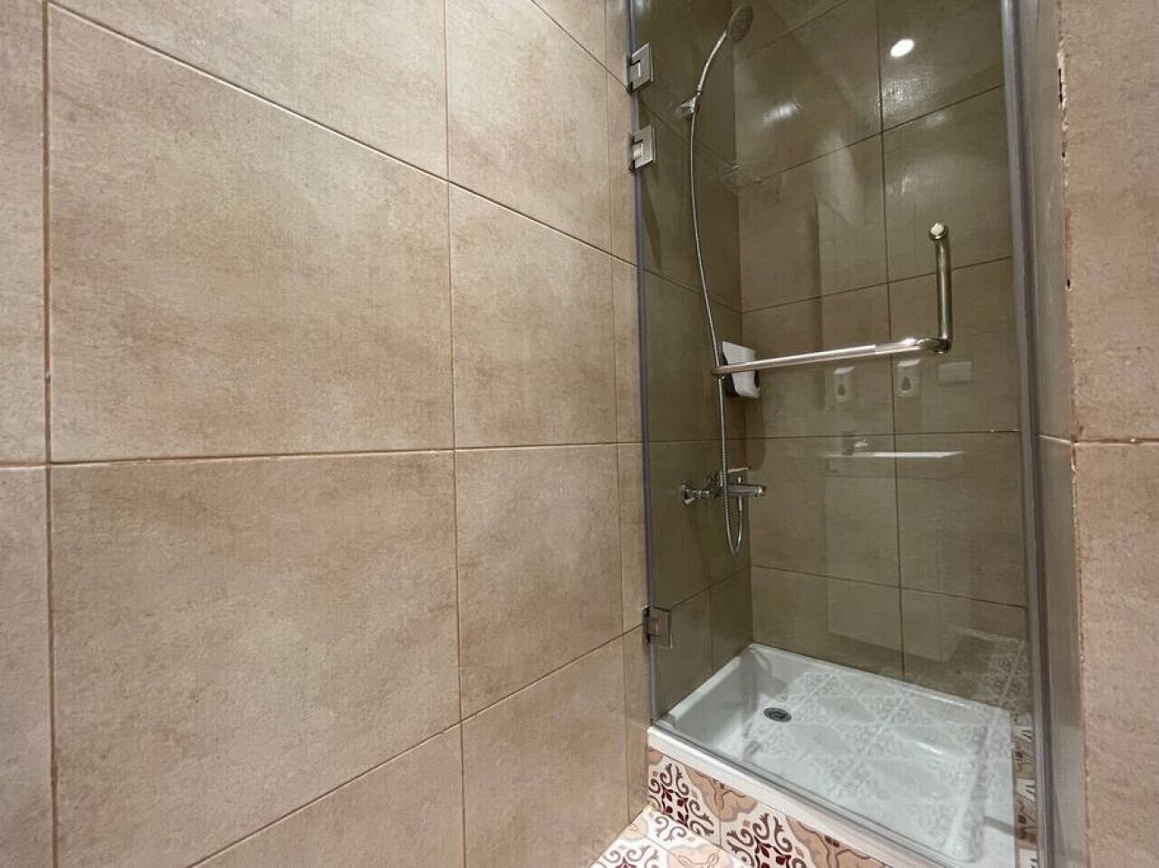 A glass-enclosed shower with a handheld showerhead and a handheld faucet.
