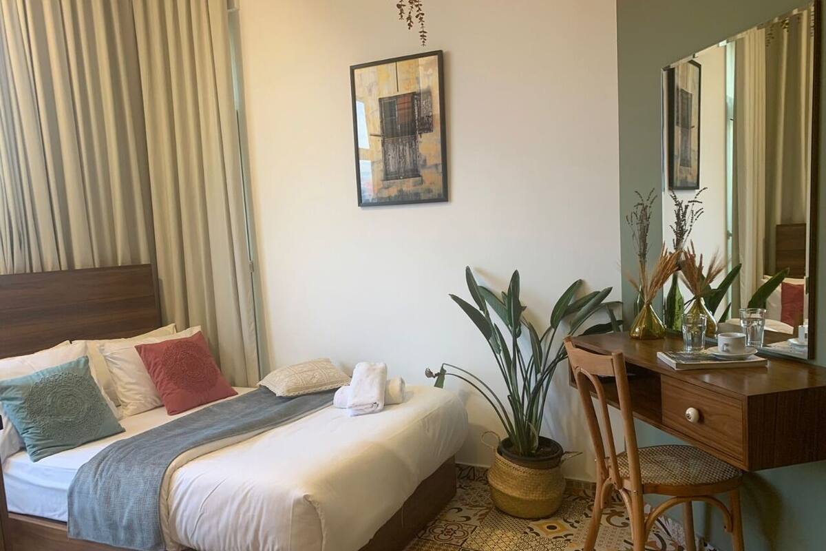 A neatly made bed with pillows, a bedside table with a vase and a mirror, and a potted plant.