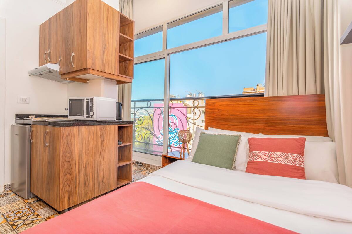 A hotel room with a bed, a wooden wardrobe, a microwave, and a balcony with a view.