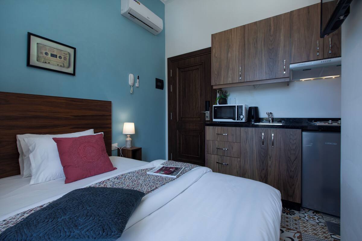 A hotel room with a bed, a nightstand with a lamp, a microwave, and wooden cabinets.