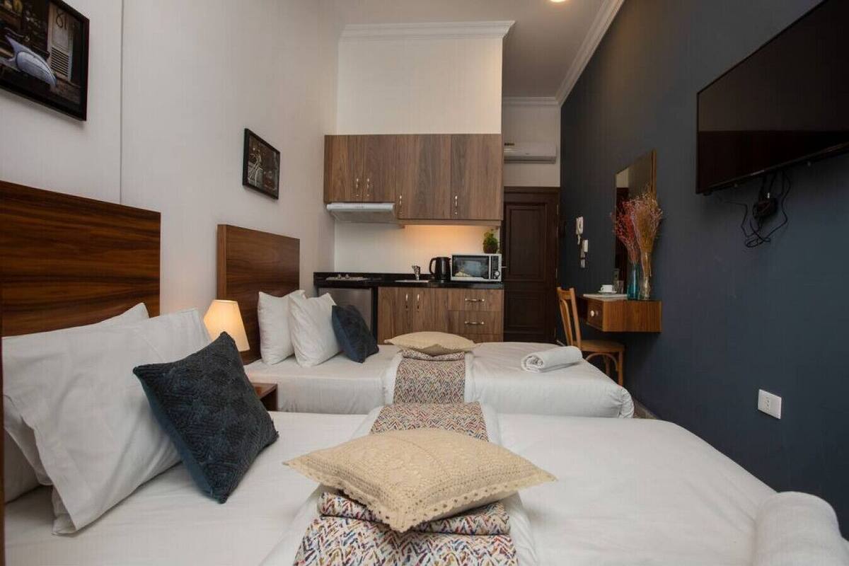 A hotel room with two beds, a kitchenette, a TV, and a dark-colored wall.