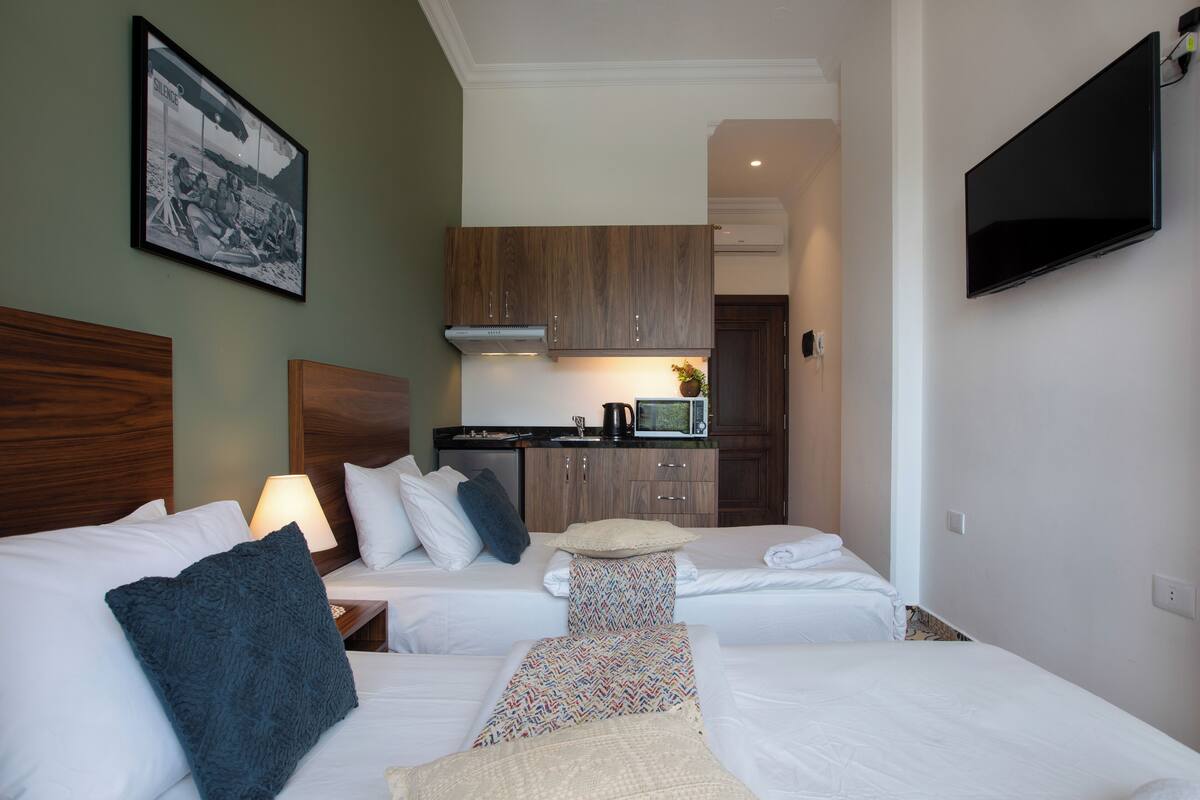 A hotel room with two beds, a kitchenette, a flat-screen TV, and a framed picture on the wall.