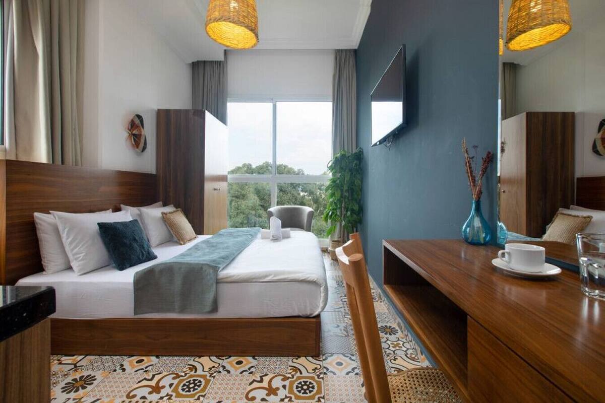 A hotel room with a bed, a desk, a chair, a TV, and a view of the outdoors.