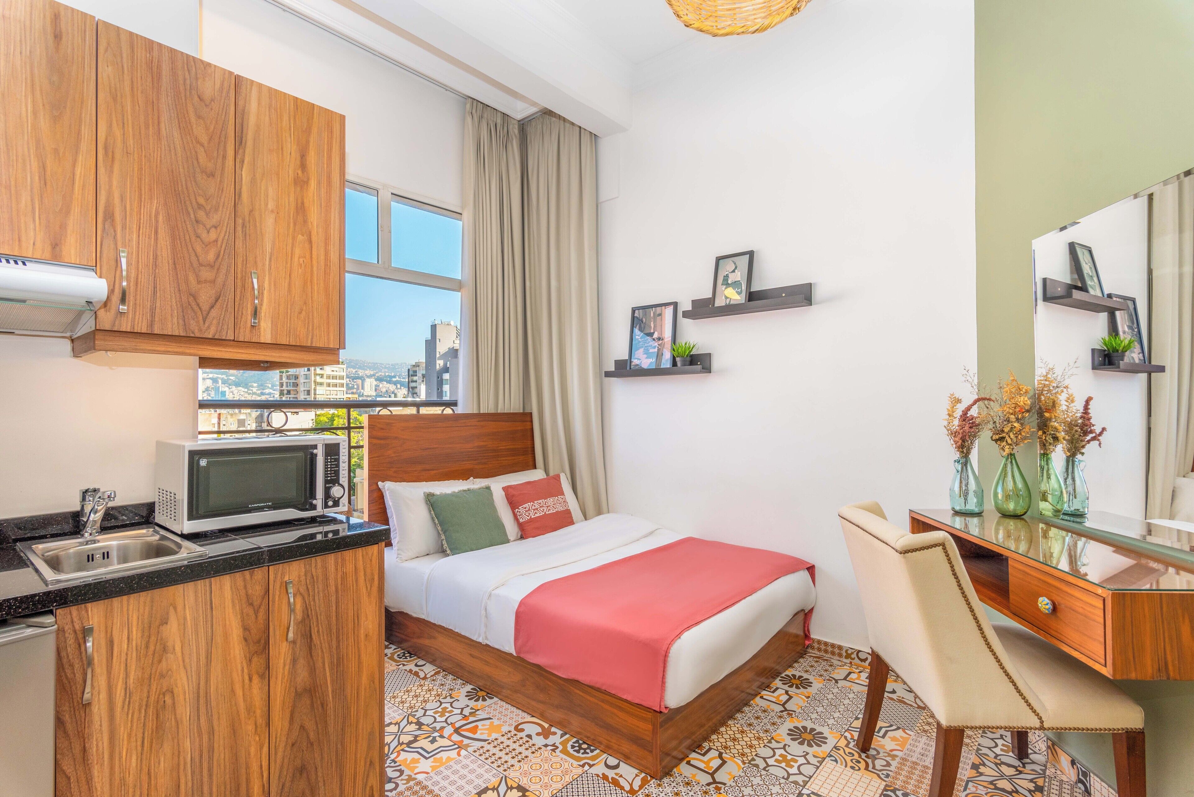 Ein Hotelzimmer mit Bett, Schreibtisch, Mikrowelle, Spüle und Blick auf die Stadt.