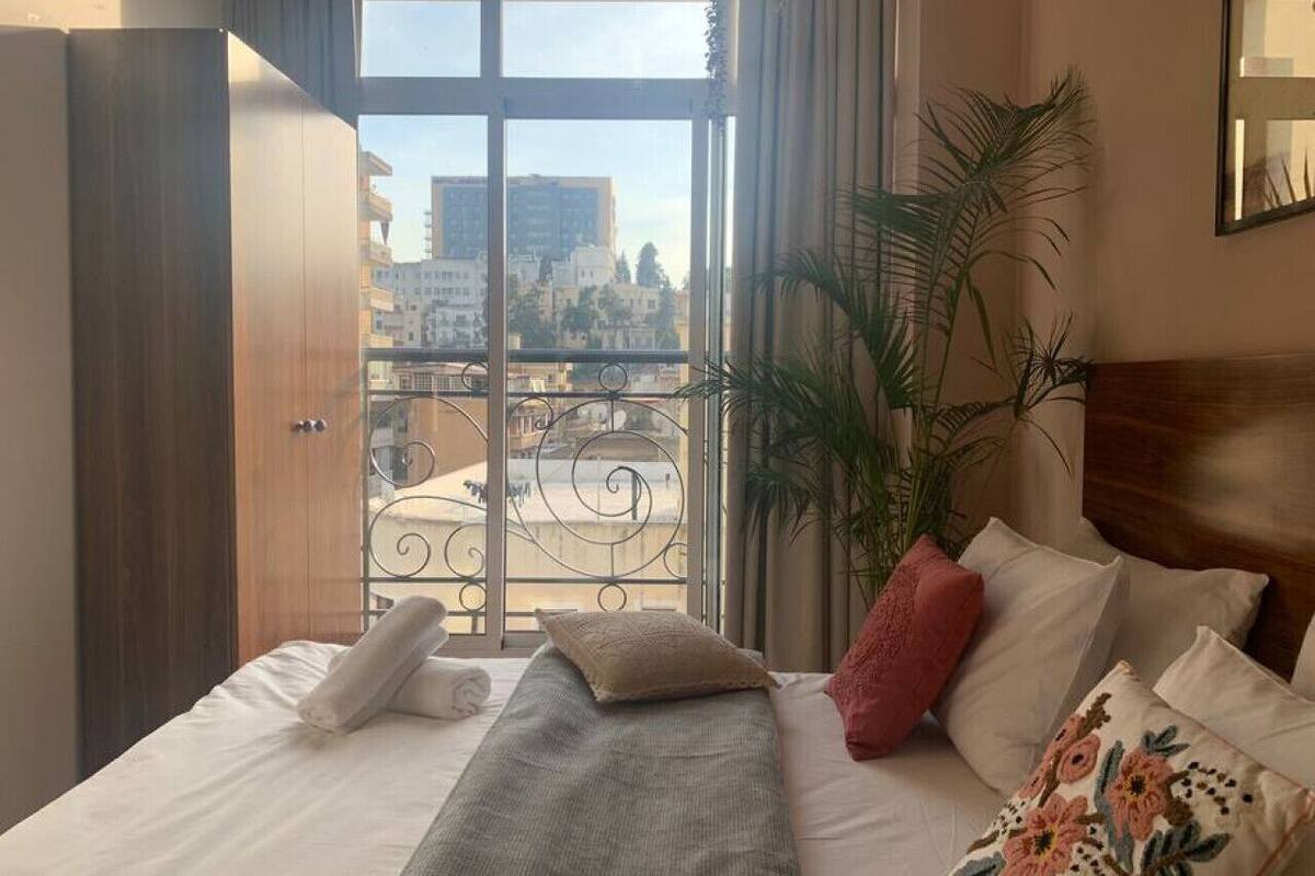 A hotel room with a bed, a balcony with a wrought iron railing, and a view of the cityscape.