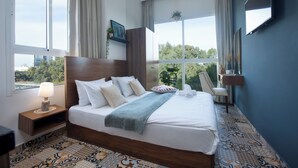 A hotel room with a large bed, a nightstand, a TV, and a view of the outdoors. - Mar Mikhael Studios (Beirut)