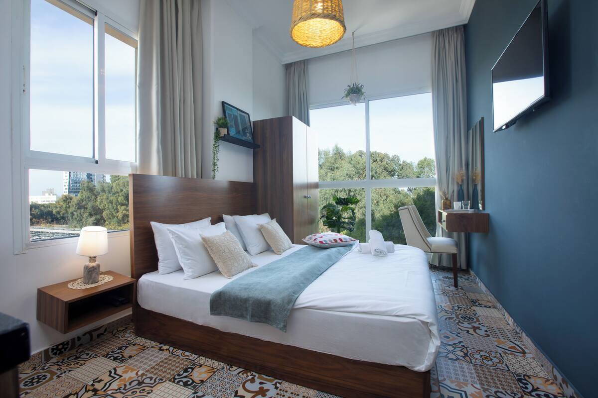 A hotel room with a large bed, a nightstand, a TV, and a view of the outdoors.