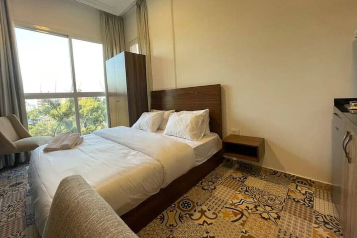 A hotel room with a large bed, a chair, a nightstand, and a view of the outdoors.