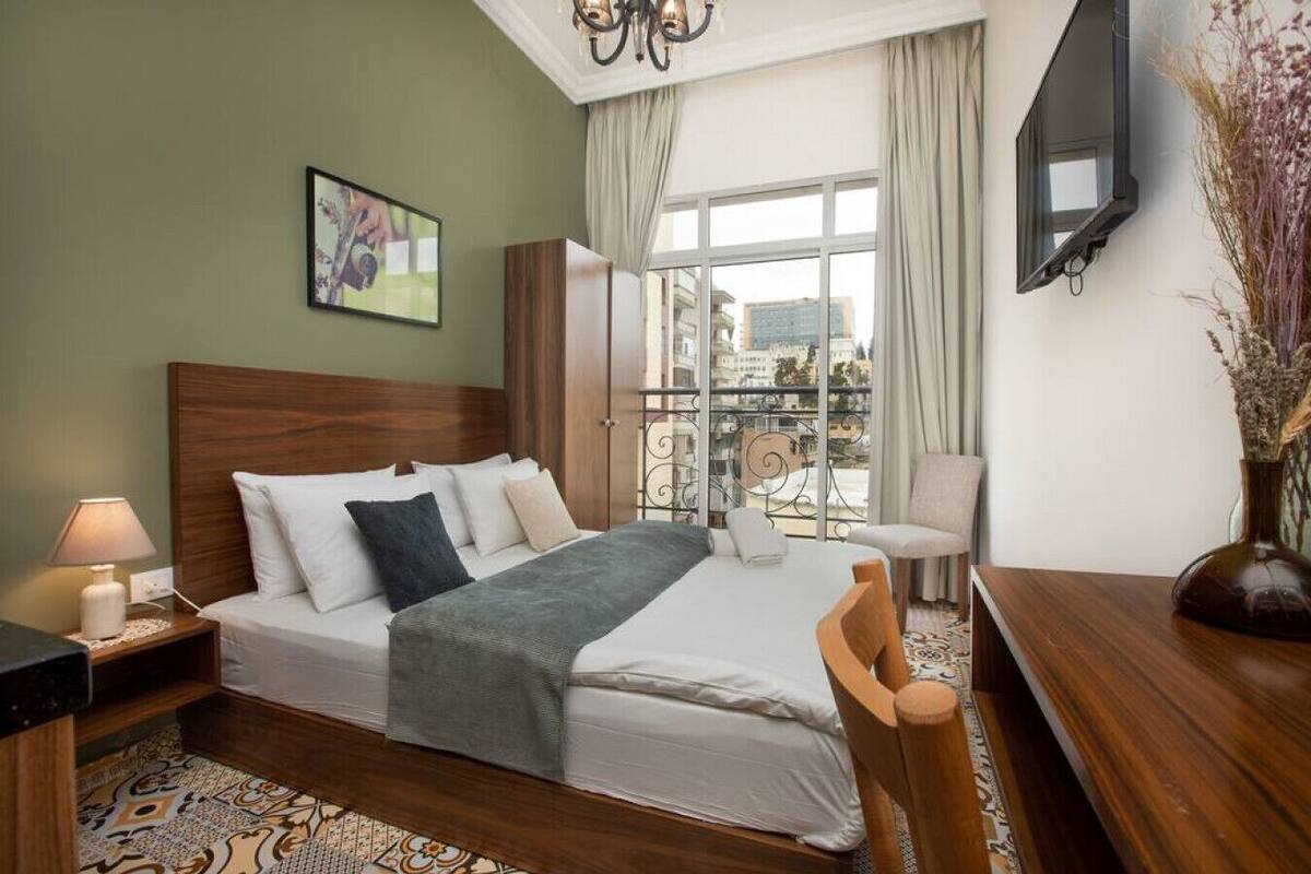 A hotel room with a bed, a desk, a chair, a TV, and a window with a view of buildings.