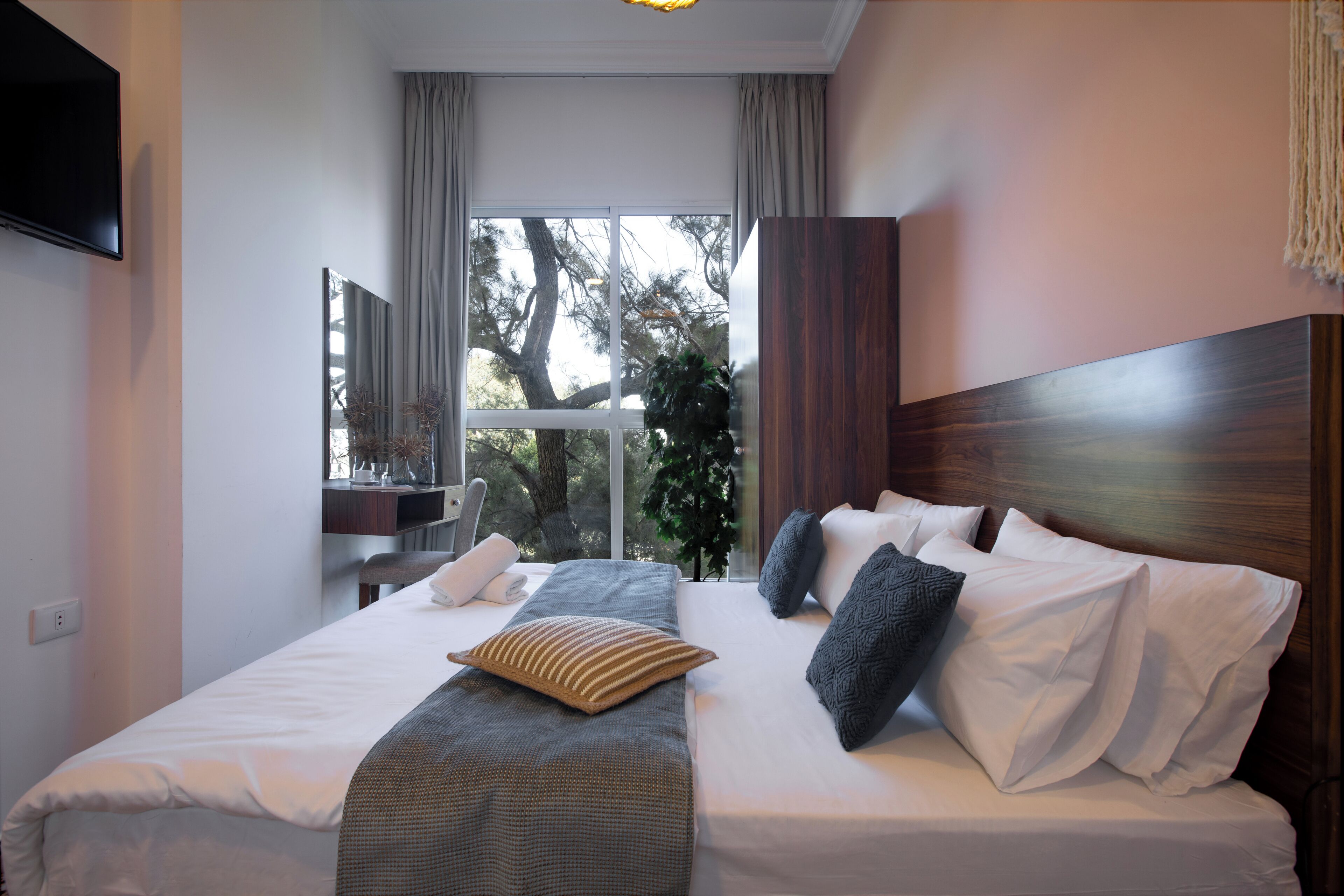 Camera d'albergo con un letto grande, una televisione montata a parete e una finestra con vista sugli alberi.