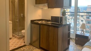 A compact kitchen with dark wood cabinets, a black countertop, and a view of the city through large windows. - Mar Mikhael Studios (Beirut)