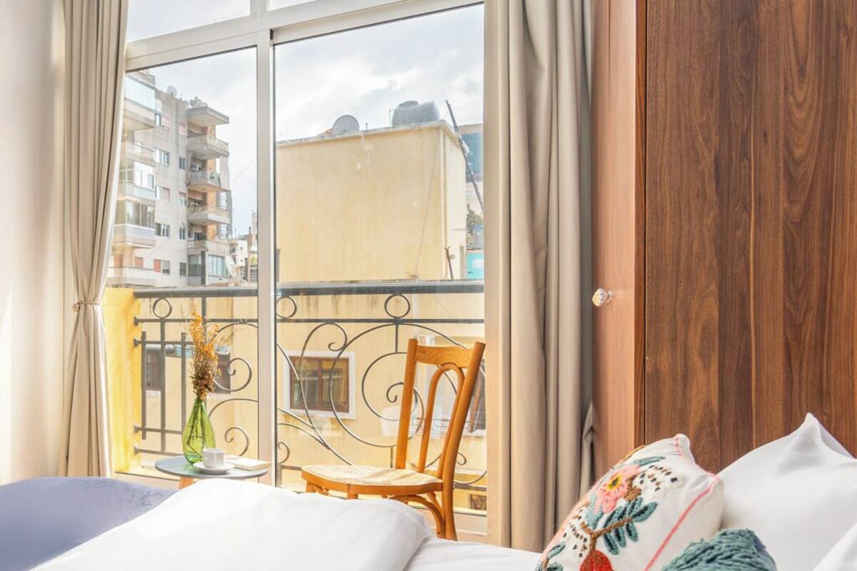 A hotel room with a large window, a balcony with a chair, and a wooden wardrobe.