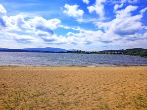 A beach with a lake, distant mountains, and a partly cloudy sky.