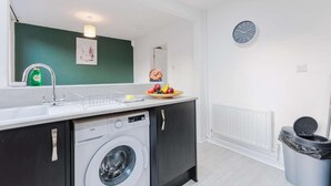 Una cocina compacta con lavadora, un lavamanos y un reloj en la pared.