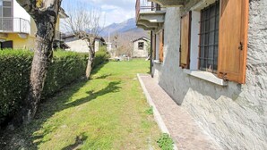 A narrow pathway leading to a building with a stone facade and wooden shutters.