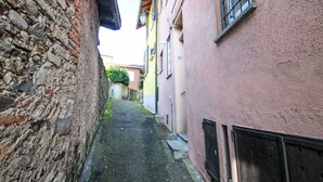 A narrow alleyway between buildings with stone walls on one side and a pink building on the other. - Cosy apartment for 2 guests with WIFI and TV (Castelveccana)