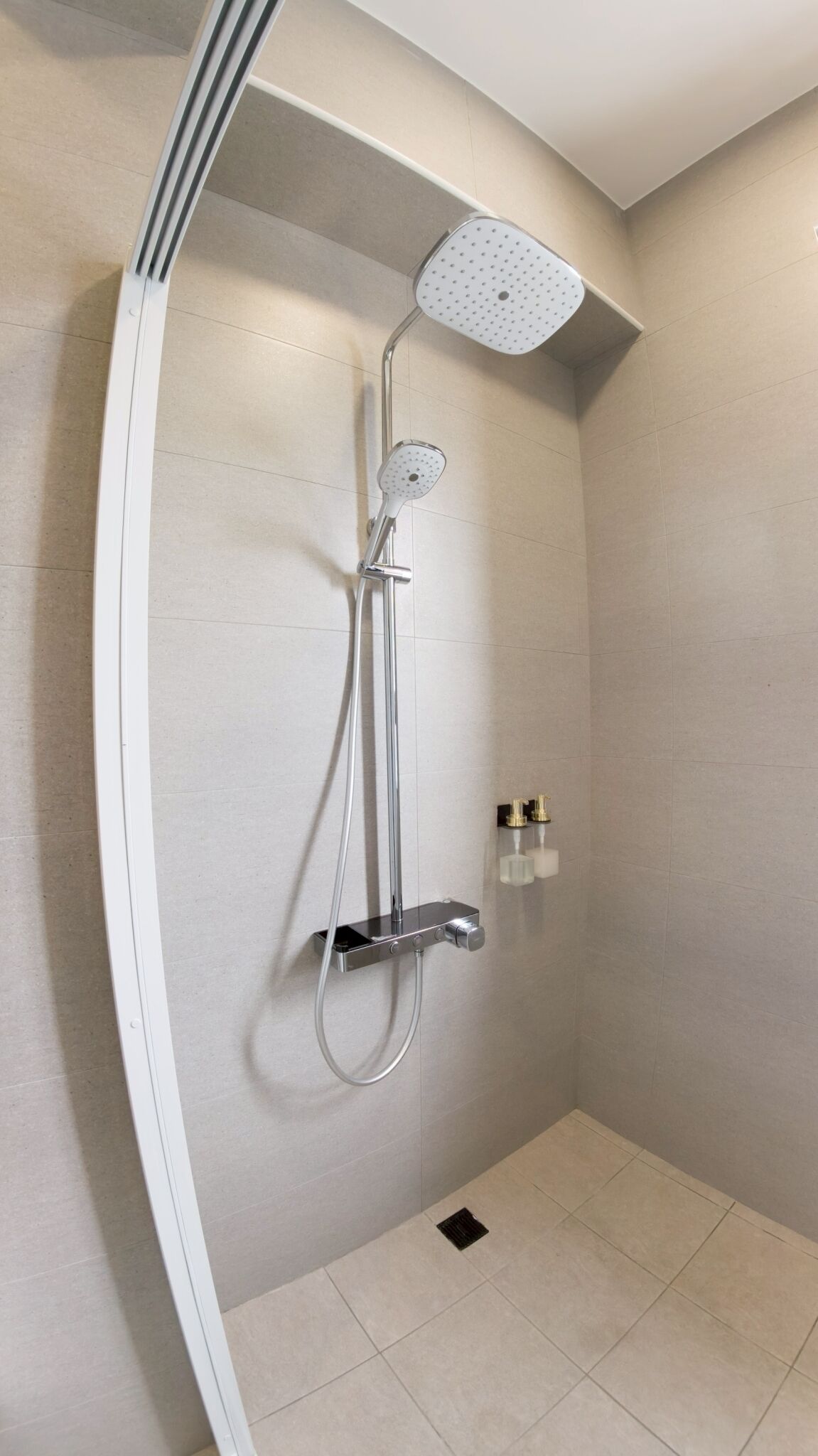 A modern shower with a handheld showerhead and a fixed overhead showerhead, a control panel, and two bottles of shampoo and conditioner.