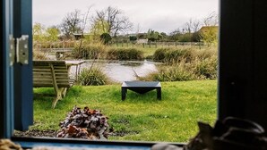 A view from a room with a door leading outside. There is a grassy area with a bench and a small table. A pair of shoes is visible on the floor. - Shepherd's Hut- Hot Tub- Wellness Spa- Wood Burner (Nottingham)