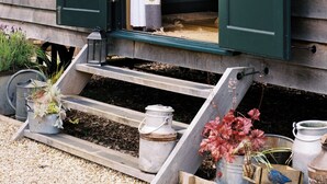 A rustic wooden building with a bed, a staircase leading to the entrance, and a small porch area with potted plants. - Shepherd's Hut- Hot Tub- Wellness Spa- Wood Burner (Nottingham)