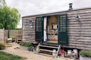 Ein rustikales Holzhaus mit sichtbarer Küchenzeile durch offene Türen, ausgestattet mit einem Holztisch, Stühlen und einer Hängelampe.