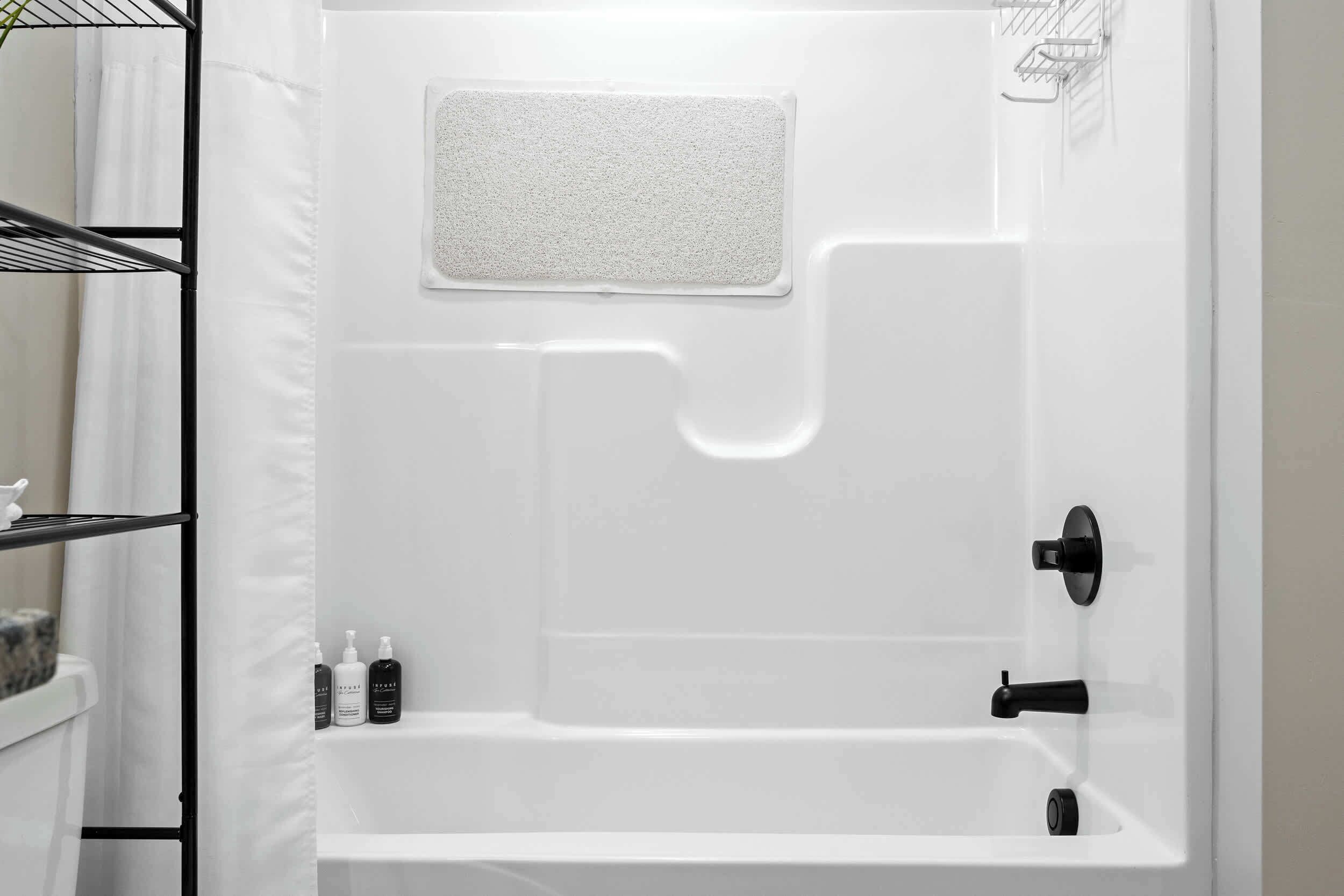 A modern bathroom with a white bathtub, a shower area, and a shelf with toiletries.