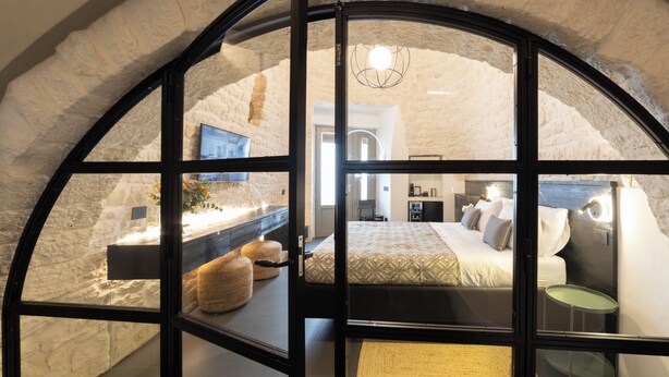 A bedroom with a bed, bedside tables, and a view through a window. - Trullo delle Sfere, Luxury Trullo in the center of Alberobello (Alberobello)
