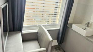 A bathroom with a bathtub, a window with blinds, and a shower area.