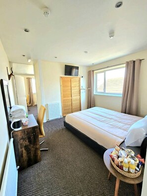 A hotel room with a bed, a desk, a chair, a television, a window with curtains, and a small table with food and drinks. - Hotel Claytou (Blackpool)
