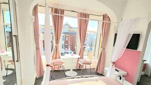 A room with a large bed, a small table, two chairs, and a window with curtains.