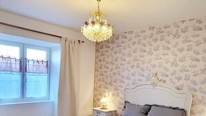 A bedroom with a large bed, a chandelier, a nightstand with a lamp, and a window with curtains. - TBM gîte country house completely renovated and quiet (Clamerey)