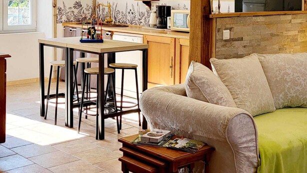 A cozy living room with a sofa, a dining table with chairs, a wooden beam structure, and a kitchen area in the background. - TBM gîte country house completely renovated and quiet (Clamerey)