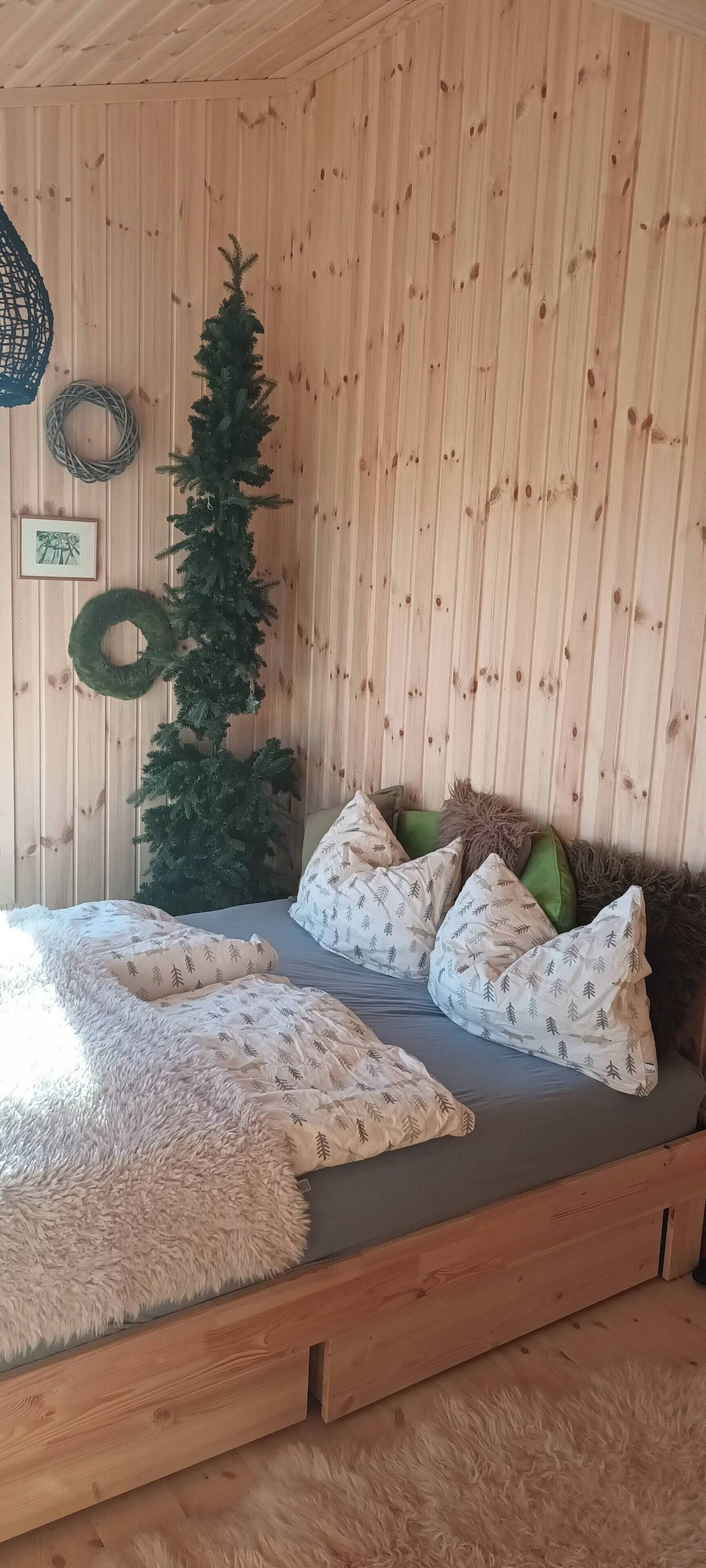 Una habitación acogedora con una cama de madera, un pequeño árbol de Navidad y una pared decorada con un adorno y una fotografía.