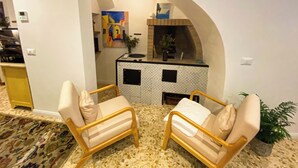A cozy living area with two beige armchairs, a small coffee table, and a kitchen area with a tiled backsplash and a hanging light fixture. - Caramia srls (Crispiano)