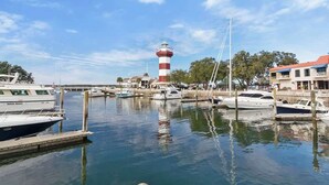 Un port de plaisance avec des bateaux amarrés, un phare et des bâtiments en arrière-plan.