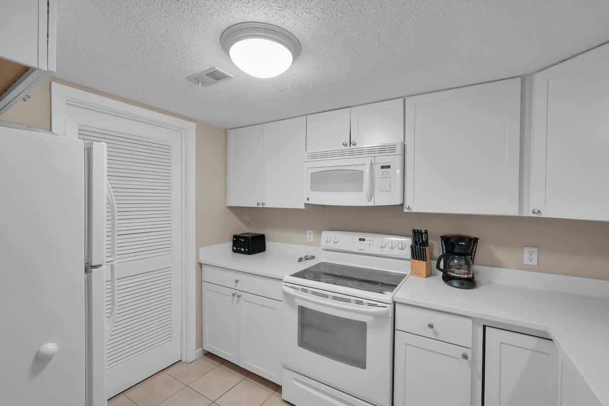 A compact kitchen with white cabinets, a microwave, a stove, and a coffee maker.