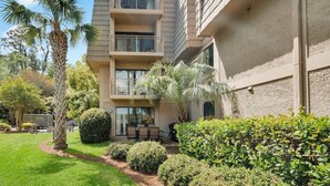 Un immeuble résidentiel à plusieurs étages, doté de balcons, d’un jardin bien entretenu et offrant une vue sur un ciel dégagé.