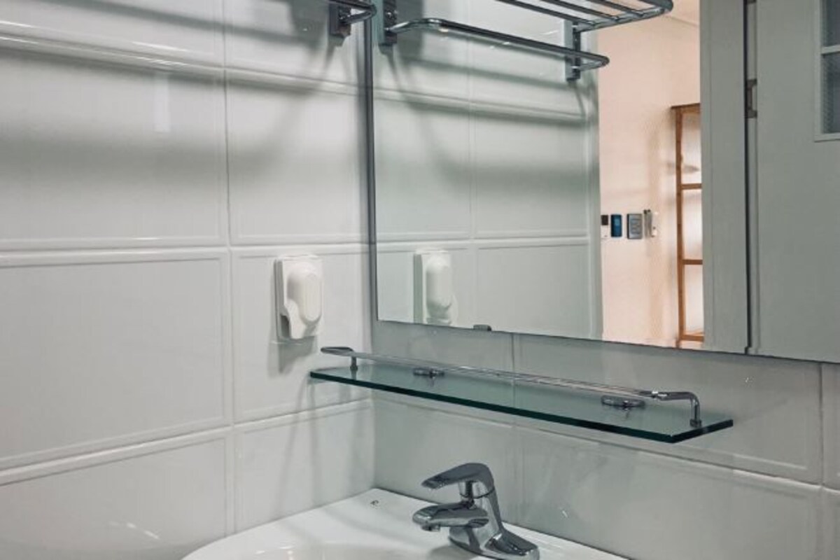 A bathroom with a glass shelf above the sink, a mirror, and a towel rack.