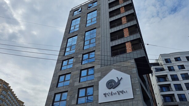 A modern building with a prominent sign featuring a snail logo and Korean text. - Red hat snail (Seogwipo)