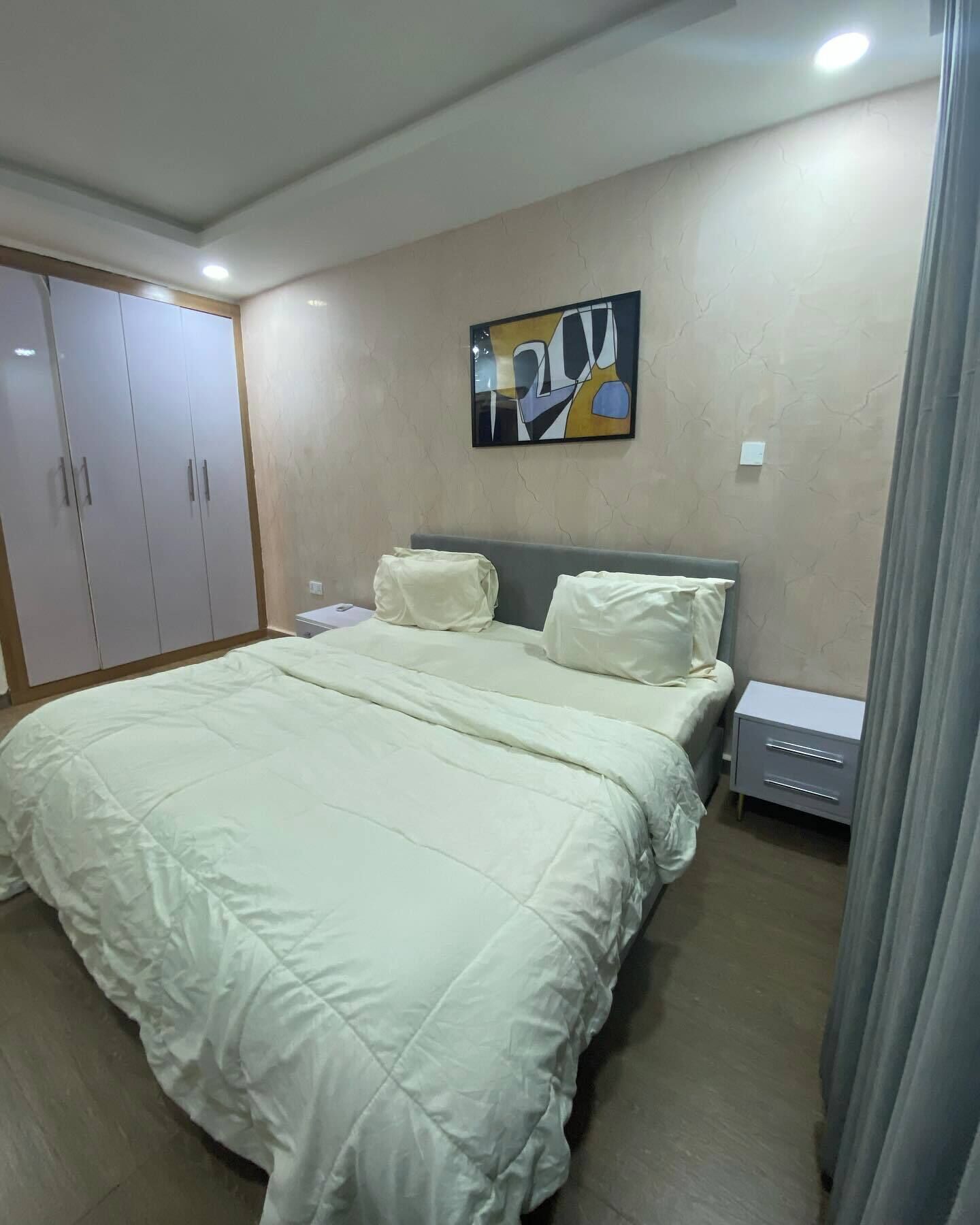 A bedroom with a bed, a nightstand, a wardrobe, and a painting on the wall.