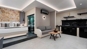Un espacio habitable moderno con una pared de piedra, un sofá, una mesa de centro con fruta y una zona de cocina con armarios negros y una encimera de mármol.