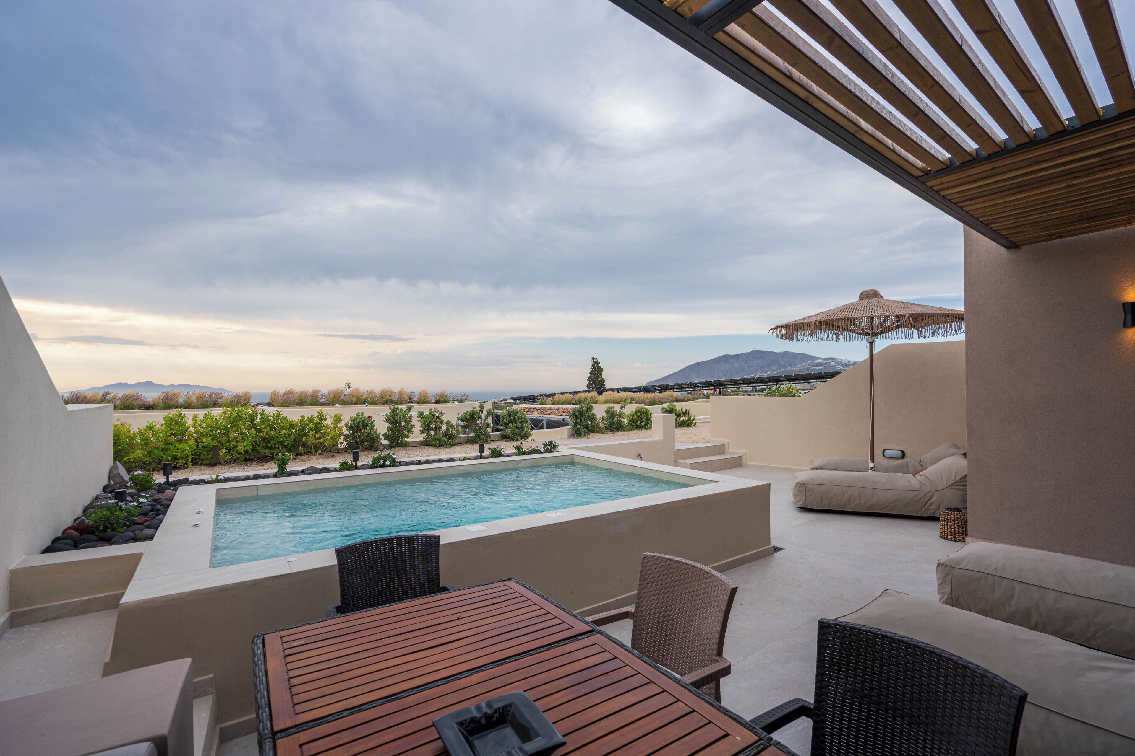 A rooftop pool with a view of mountains, outdoor furniture, and a pergola.